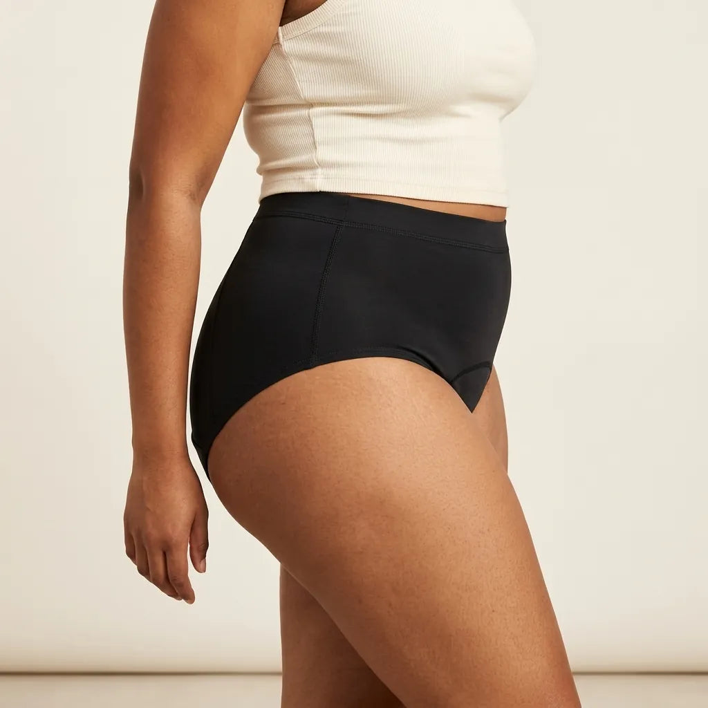 Side view of a woman wearing the black Insoucia high-waisted period brief, showing the wide side panel and the reinforced side seam.